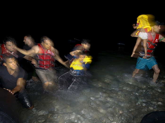 Syrian refugees carry their children as they jump off a dinghy overcrowded with Syrian refugees upon arriving on a beach on the Greek island of Kos, August 9, 2015.