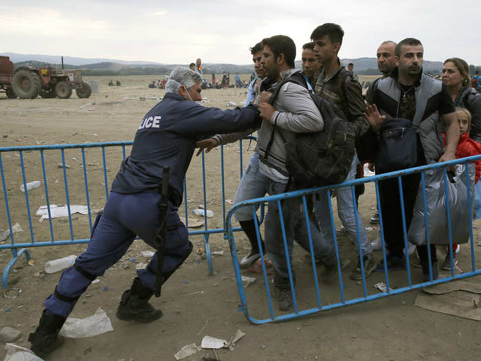 A Greek policeman pushes refugees behind a barrier at Greece