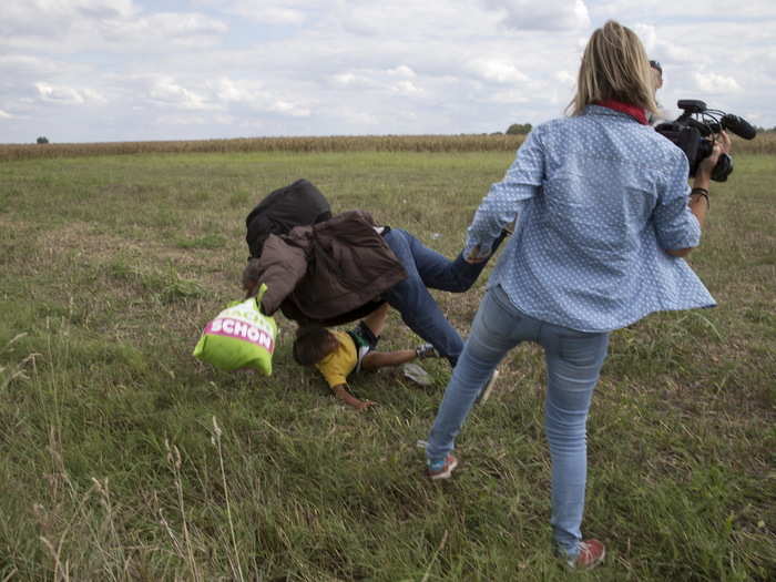 A refugee carrying a child falls after tripping on TV camerawoman (R) Petra Laszlo while trying to escape from a collection point in Roszke village, Hungary, September 8, 2015.