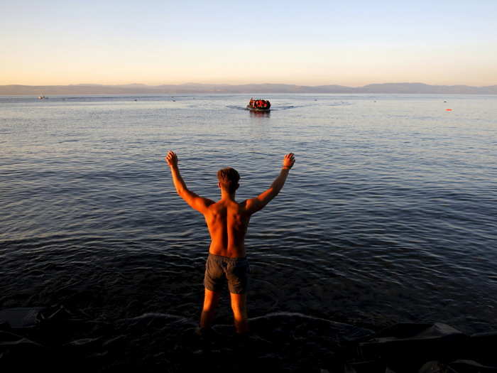 A local volunteer signals to refugees overcrowding a dinghy to approach at a beach on the Greek island of Lesbos after crossing a part of the Aegean Sea from Turkey (seen in the background) September 18, 2015.