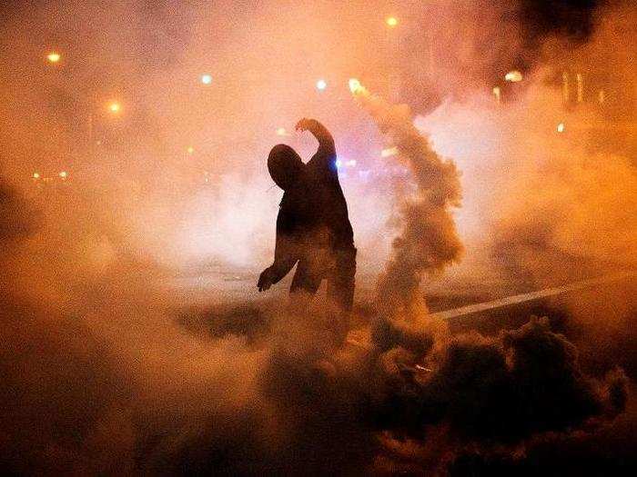 A protester throws a tear gas canister back toward riot police after a 10 PM curfew went into effect in the wake of riots following the funeral for Freddie Gray on April 28, 2015, in Baltimore. Gray suffered a spinal injury in police custody and later died, sparking unrest in the city.