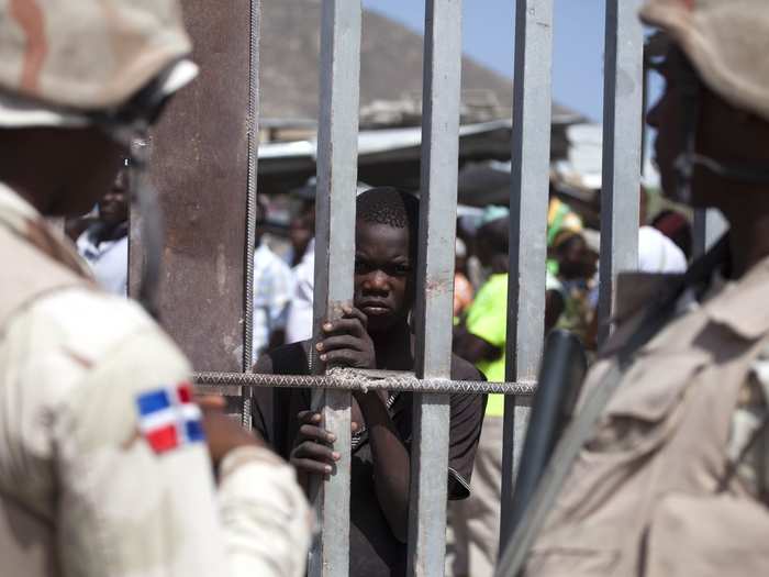 DOMINICAN REPUBLIC: In this August 4, 2015 photo, a Haitian youth peers from behind a border fence separating the Haitian town of Malpasse and the Dominican Republic town of Jimani.