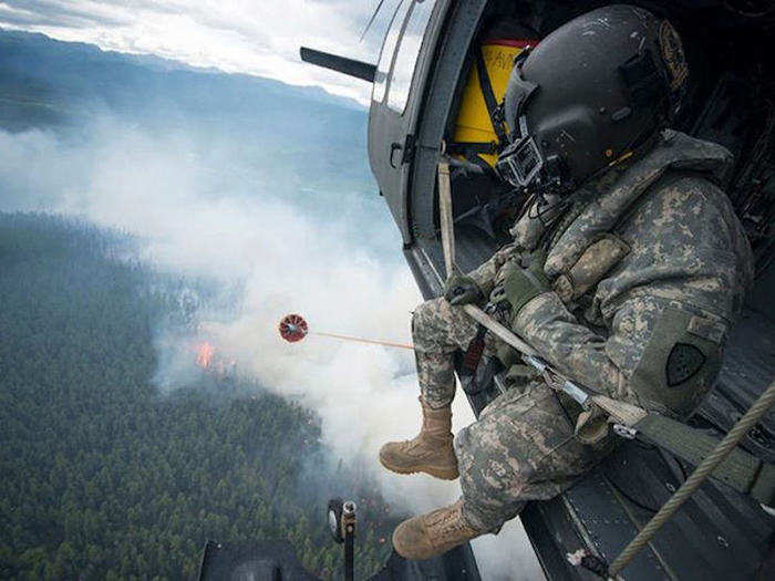 June 26: A U.S. Army? UH-60 Blackhawk helicopter crew chief, assigned to the Alaska National Guard, conducts water bucket operations during a fire-fighting mission south of Tok, Alaska. Two UH-60 helicopters aided in fighting the wildfire in coordination with the Bureau of Land Management, Fire Services based out of Fort Wainwright, Alaska.