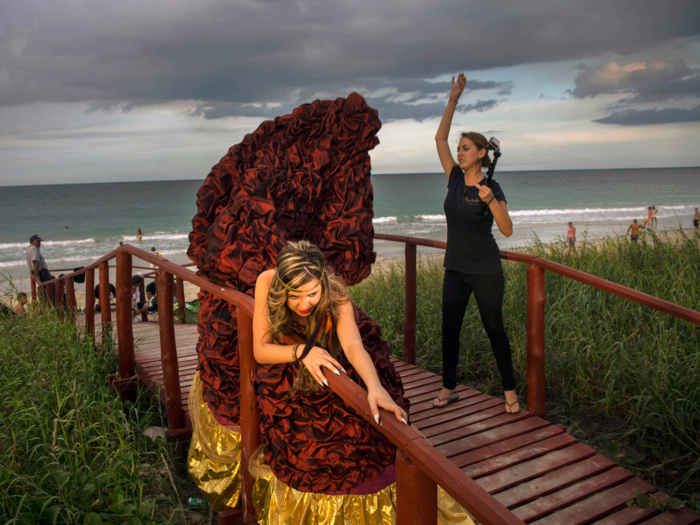 Camila Lopez Rivas poses on a beach in Havana while an assistant lifts the train of her dress to make it seem as if it