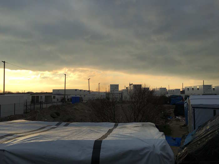 The sun sets on the shelters and tents in which most of the 5,000 inhabitants of the Jungle live. In the background are the white shipping containers where the French government intends to house around 1,500 refugees.