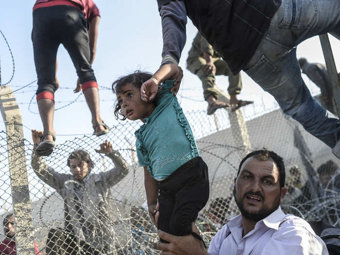 Spot News Stories, 3rd prize: Bulent Kilic, Turkey — A refugee man holds a young girl as others climb over broken-down border fences to enter Turkish territory; Sanliurfa, Turkey, 14 June 2015.