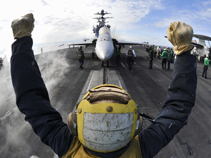 An aircraft director guides an F/A-18C Hornet onto a catapult aboard the aircraft carrier USS Harry S. Truman.