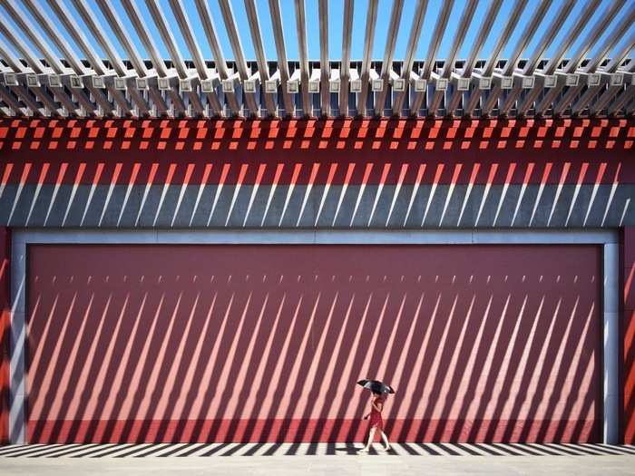 A woman walks in front of a red wall in China.