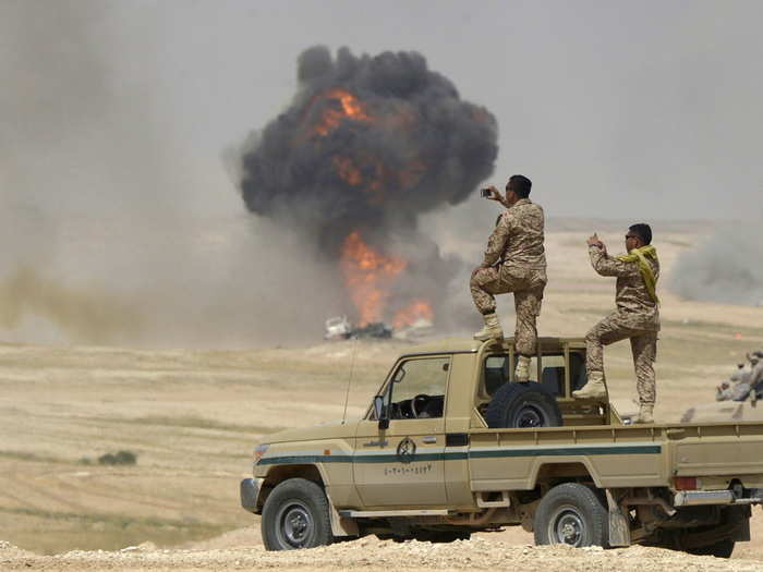 Soldiers take pictures as flame and smoke are seen following air bombardments during the Northern Thunder multinational military exercises, in Hafr Al-Batin, near Saudi Arabia