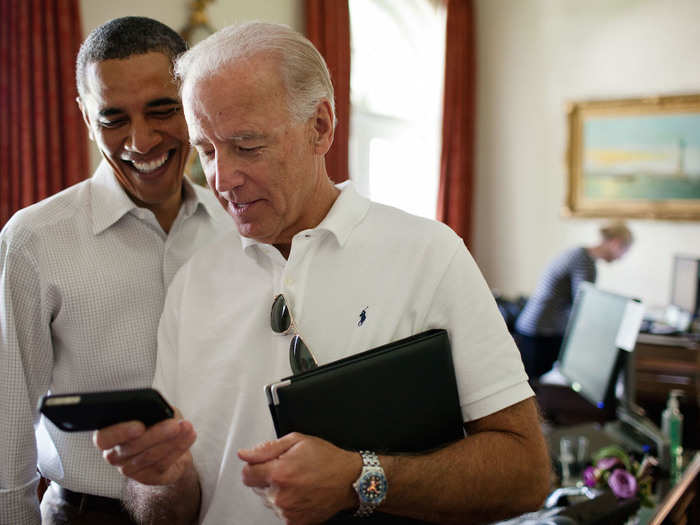 Biden and Obama look at an app on an iPhone in the Outer Oval Office.
