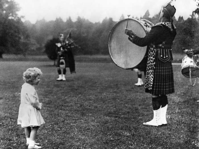 1929: In this photo, a curious Princess Elizabeth watches on as a Highland Regiment drummer performs in the grounds of Balmoral Castle.