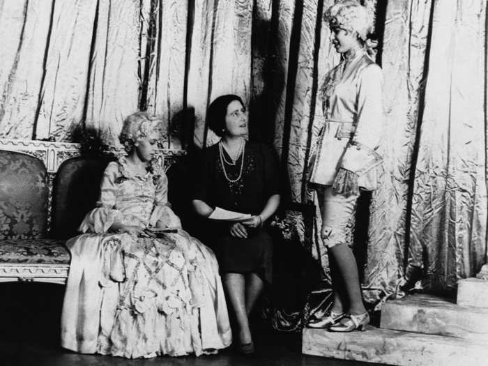 1941: Princess Elizabeth discusses the pantomime with her mother, Queen Elizabeth of England, while her sister, Princess Margaret, looks on.  The two princesses took the leading roles in the show and also produced the play for the benefit of the Royal Household Concert Wool Fund.