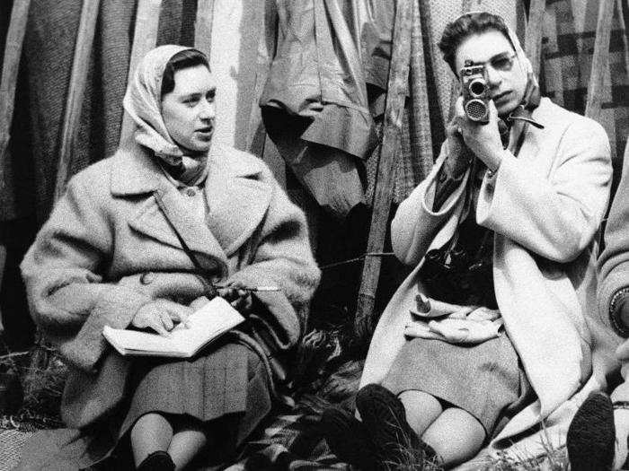 1957: In this photo, the Queen and her sister, Princess Margaret, enjoy a day out at the horse shows in Badminton, Gloucestershire. The queen is holding an old-fashioned movie camera as she takes pictures of the cross-country competition.