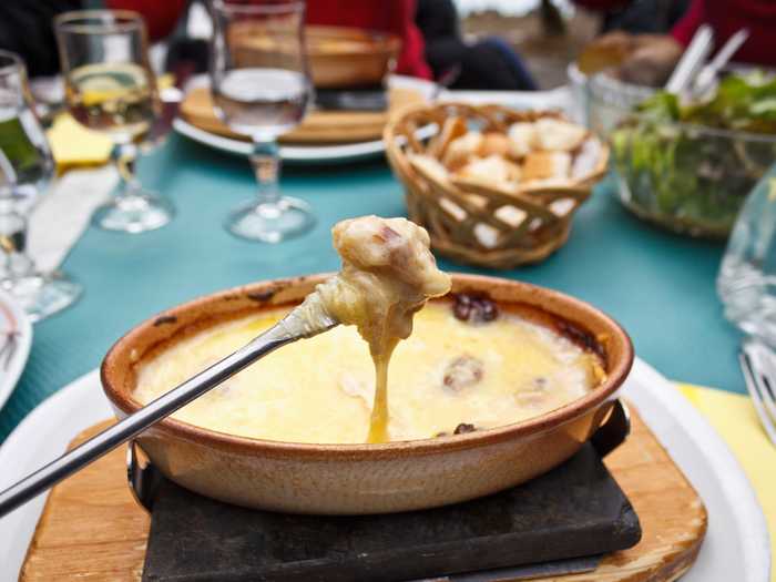 Fondue is the national dish of Switzerland. It consists of Emmental and Gruyère cheeses, melted in a pot with white wine, garlic and lemon. Long-stemmed forks dip bread, vegetables, and charcuterie into the cheesy goop, which is kept hot over a small flame.