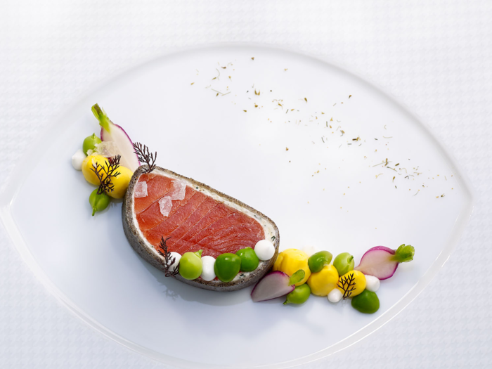 The menu also typically includes two fish courses. This plate includes wild king salmon served with radishes, English peas, hen egg mousse, and bronze fennel.