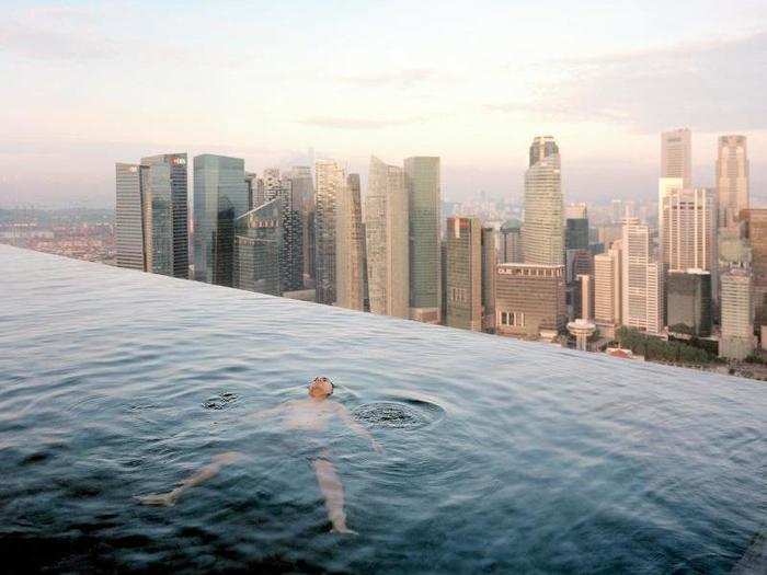 "I wanted to make a show that was made of beautiful, precious objects," Little said. In this image, a man floats in the 57th-floor swimming pool of the Marina Bay Sands Hotel, with the skyline of the Singapore financial district behind him.