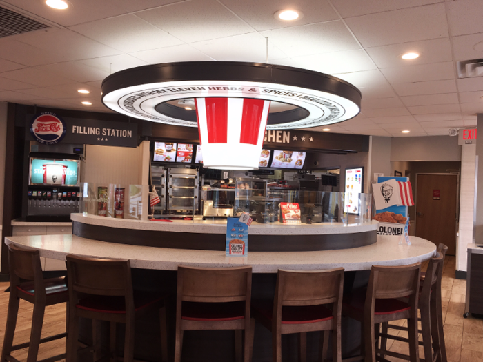 Inside, a light shaped like a bucket immediately grabs your attention — a bucket chandelier of sorts. The light hangs over a large circular table, inspired by Colonel Sanders