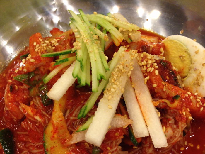 Bibim naengmyeon is a cold buckwheat noodle dish mixed with sliced beef, pickled cucumber, and spicy chili sauce.