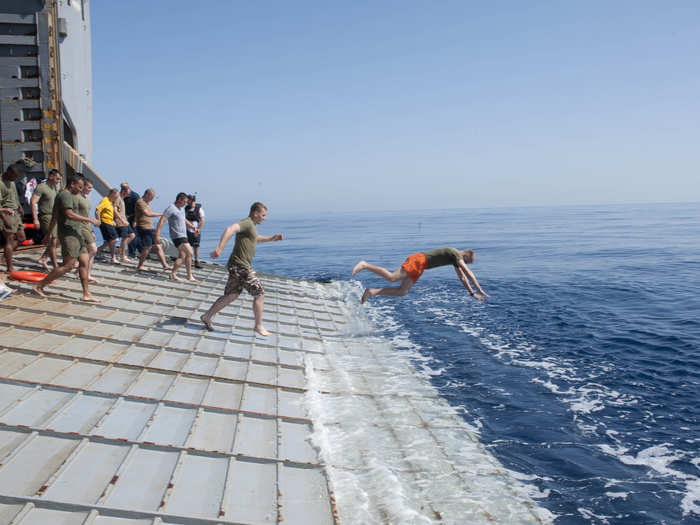 Sailors and Marines aboard the USS Fort McHenry jump off the stern gate into the Mediterranean Sea.