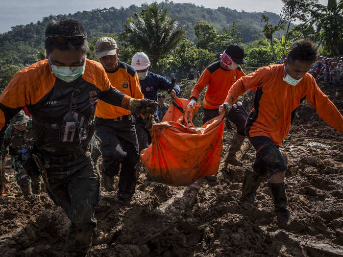 Indonesian rescue team members carry a body of a victim after a landslide in Purworejo, Indonesia. At least 47 people were killed after heavy rains and floods.