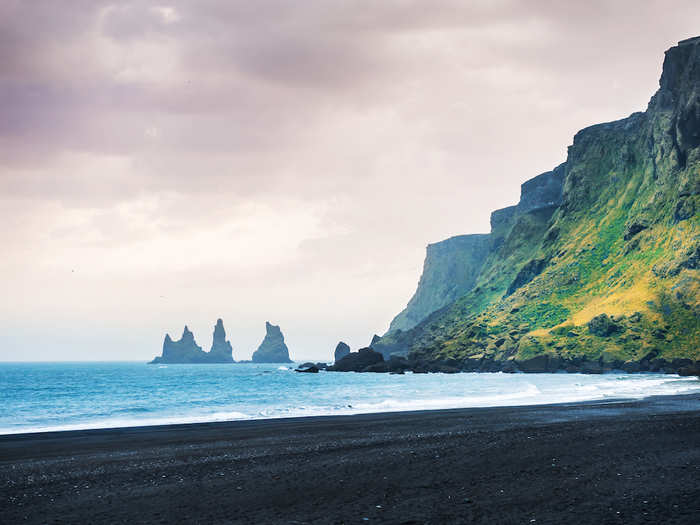 Instead of a beach with golden sand, visit Vik Beach, a dramatic black-sand beach in Iceland that is home to impressive natural rock formations.