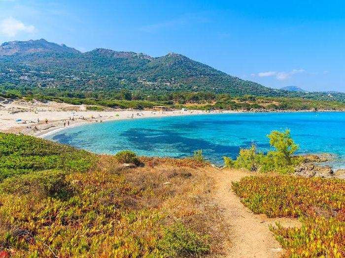 Beachgoers must traverse a slender path lined with spiky bushes to reach Saleccia beach, a quiet white-sand beach in Corsica, France.