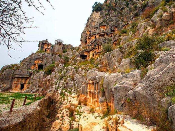 Look up at a series of intricate tombs built into the side of a mountain by the Lycians in Fethiye, Turkey.