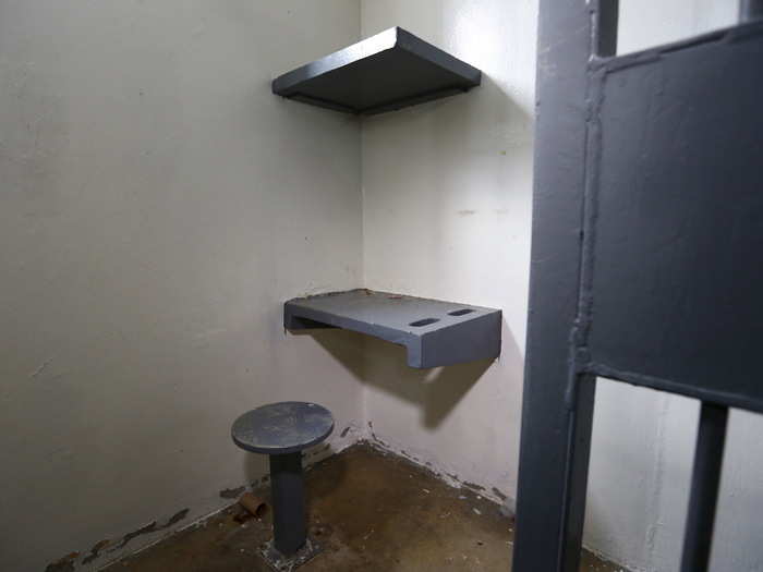 A simple desk and shelf are seen in one corner of his cell.