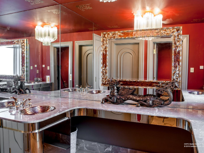 One bathroom with red walls features a granite countertop, a chandelier, and a metallic dragon holding an elaborate mirror.