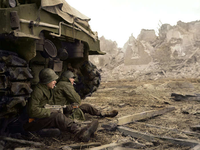 Two soldiers from C Company, 36th Armored Infantry Regiment, 9th Infantry Division, smoke cigarettes while looking out at the war-torn city of Geich, Germany.