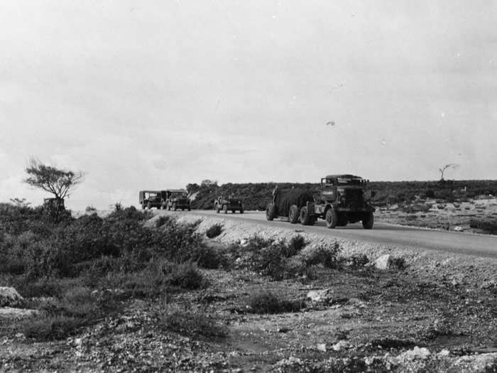 The bomb is then escorted to the nearby North Field airbase on Tinian, shrouded in tarp.