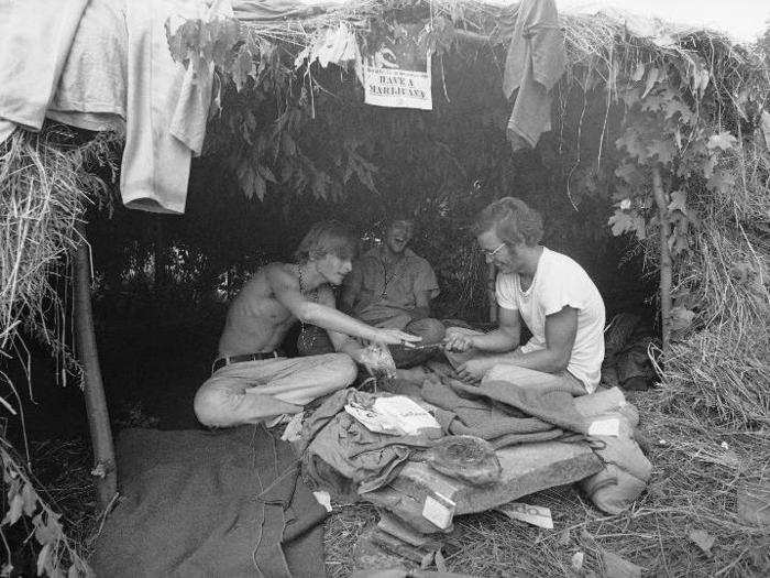 Here, three attendees relax in a grass hut. The sign above their heads reads: "Have a marijuana."