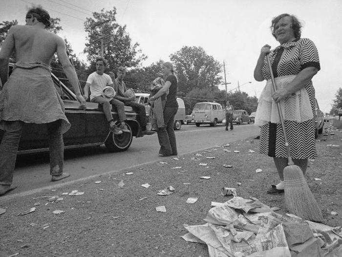 A Bethel local sweeps trash in front of her home as festival-goers make their way out of town.