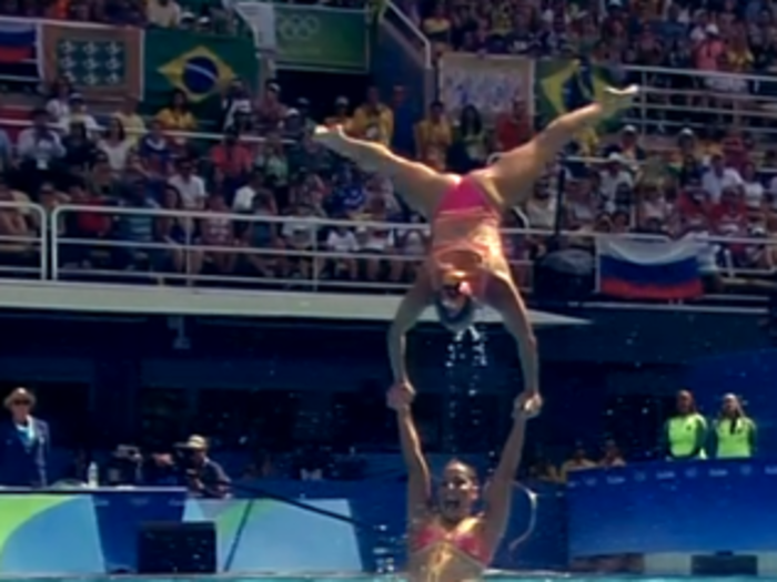 It looks like the swimmer in the handstand is being held up by just one person.