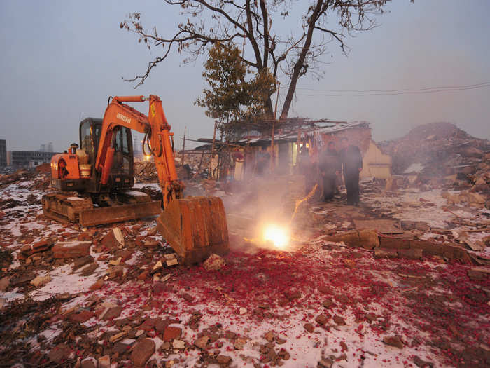 Cao Wenxia, the owner of this nail house in Hefei, lights firecrackers to celebrate the Chinese New Year. A bulldozer used to demolish nearby buildings sits ominously close.