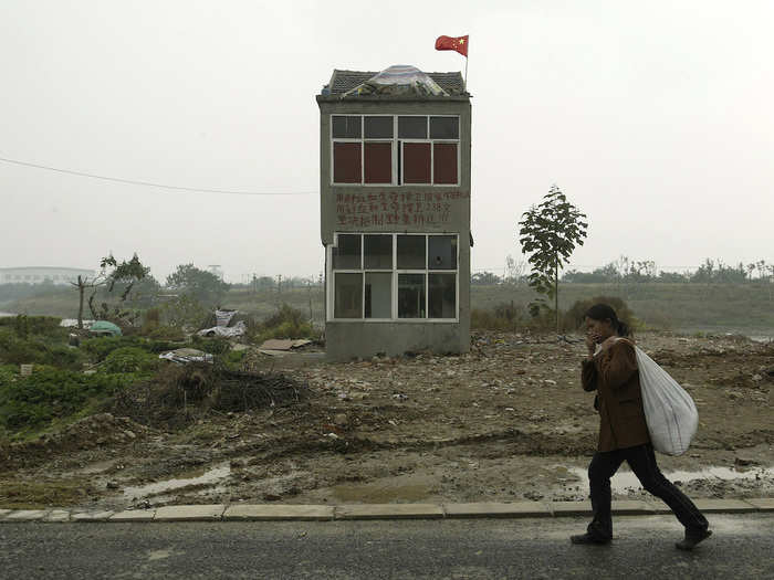 A woman walks past a “nail house” on the outskirts of Nanjing, where the land will be used for a wet land project, according to local media.