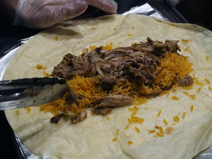 The rest of the ingredients are laid out in a similarly linear fashion. In this case, a generous portion of succulent, luscious carnitas is being laid gingerly over the carefully placed foundation of rice and beans: