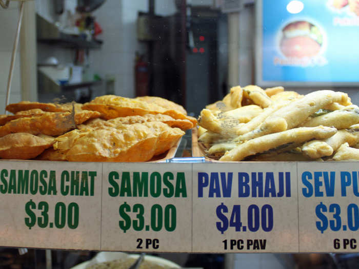 Fried Indian snacks, like samosas, are displayed behind glass in hawker centers.