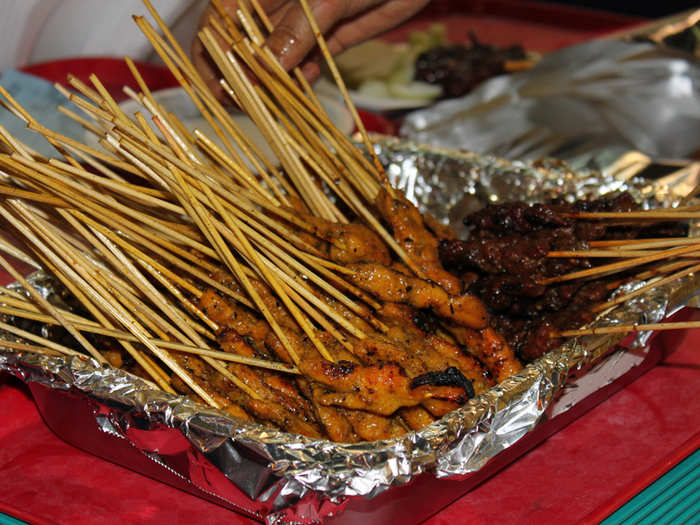 Vendors grill satay — skewers of meat — over an open flame.