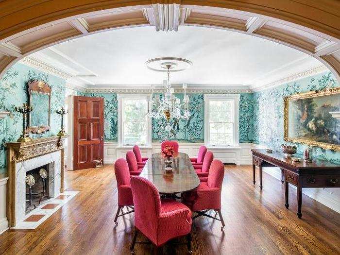 A dining room is decked out with aqua patterned wallpaper and hot pink chairs.