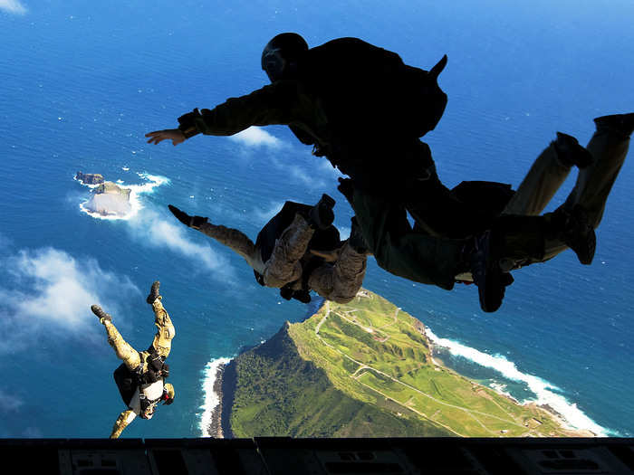 Navy SEALs leap from the ramp of an Air Force transport aircraft during parachute training over a Marine Corps base in Hawaii. Exercises like this show collaboration between military branches.