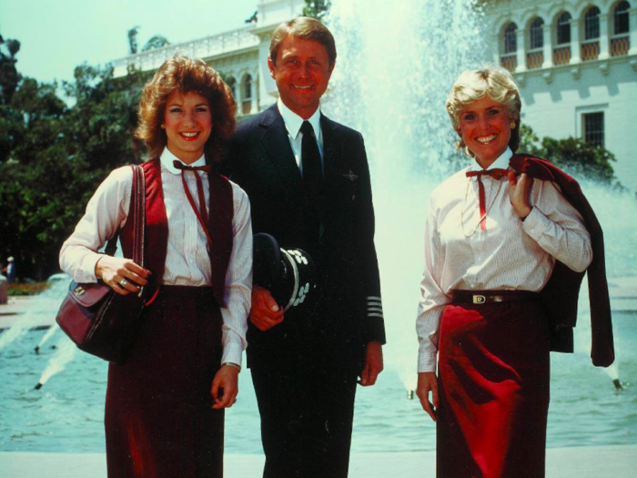 Two flight attendants and a pilot pose in front of a fountain in the 1980s.