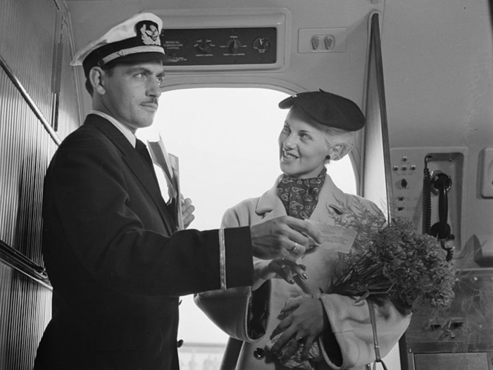 A Royal Dutch Airlines purser welcomes a passenger and points out her seat.