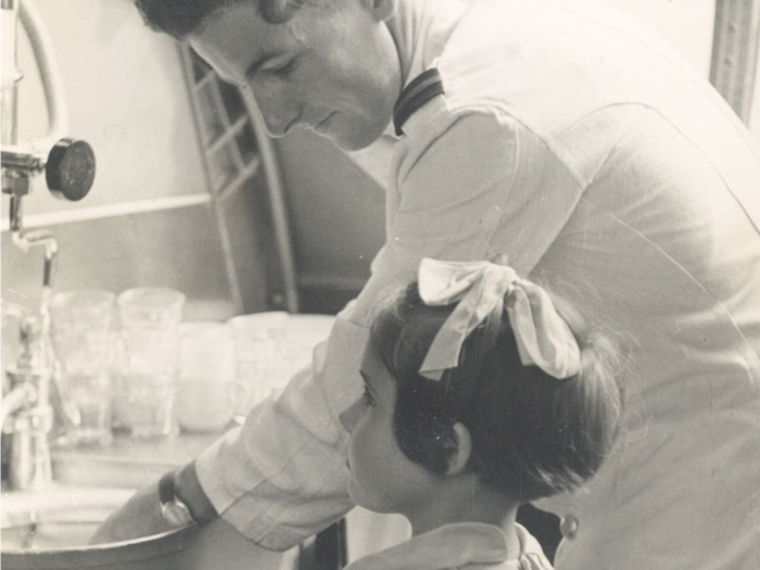 Flight steward Max White, assisted by passenger Jennifer Grey, washes dishes on board a January 1949 from Suvas to Sydney.