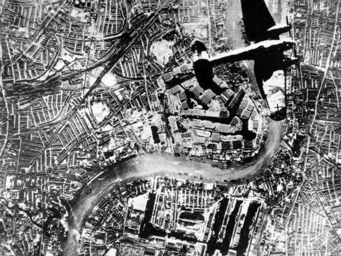 A Nazi Heinkel 111 bomber flies over London during the Battle of Britain in the autumn of 1940 during World War II. The Thames River runs through the center. The Tower Bridge is visible near the planes left wingtip.