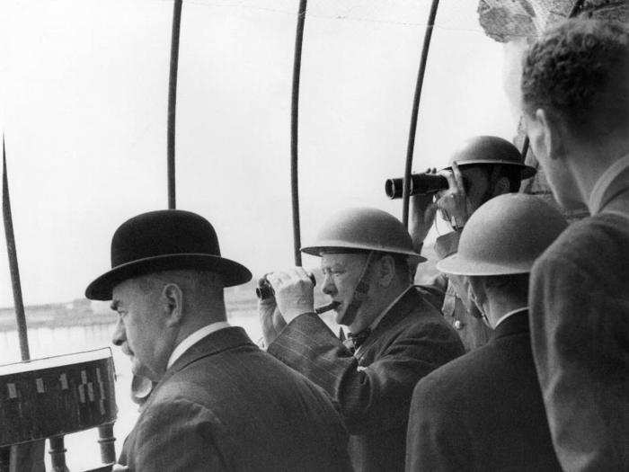 Wearing a steel helmet, English Prime Minister Winston Churchill is seen in an observation post in Dover, England, August 28, 1940, as he watched an air battle through field glasses. The mayor of Dover is shown at left.