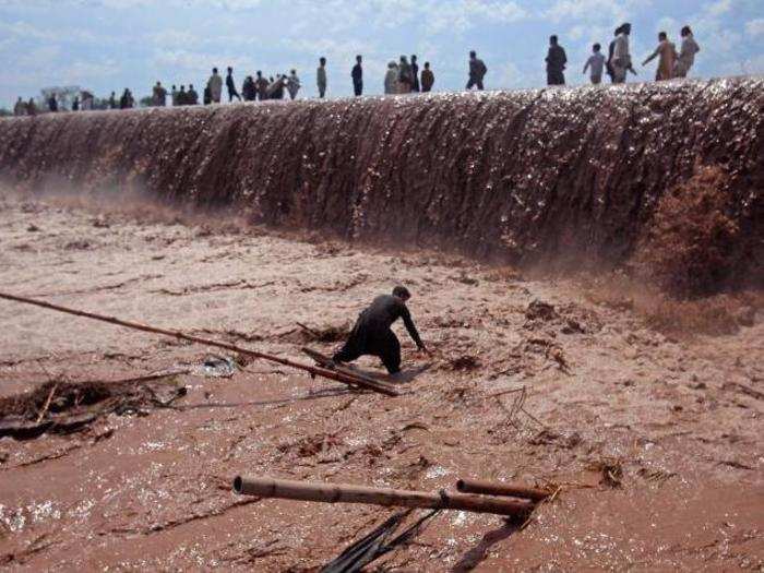 A shopkeeper tries to save his belongings as residents use a bridge covered with floodwater on the outskirts of Peshawar, Pakistan, on April 4.