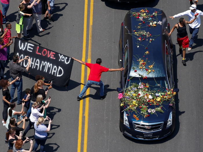 A banner stating "We Love You Muhammad" is displayed as well-wishers touch the hearse carrying the body of the late boxing champion Muhammad Ali during his funeral procession through Louisville, Kentucky.