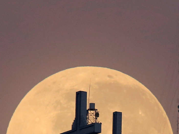 The full moon is seen behind the hill of the three crosses in Cali, Colombia.