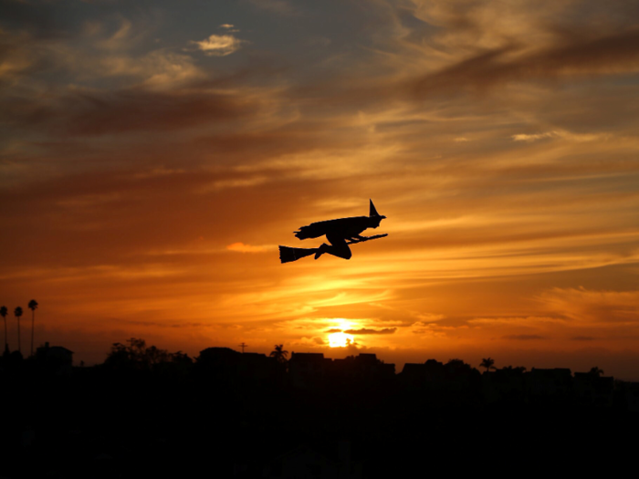 A remote-controlled plane in the form of a witch flies over a neighborhood as the sun sets during Halloween in Encinitas, California.